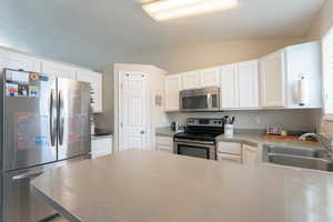 Kitchen featuring stainless steel appliances, white cabinets, vaulted ceiling, a sink, and a peninsula