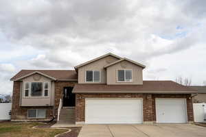 View of front of house featuring driveway, brick siding, roof with shingles, fence, and stucco siding