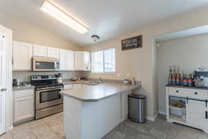 Kitchen featuring a peninsula, appliances with stainless steel finishes, a sink, and white cabinetry