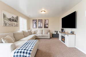 Carpeted living area with a glass covered fireplace and baseboards