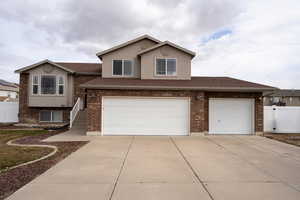 View of front of house with driveway, a shingled roof, stucco siding, fence, and brick siding