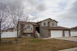 View of front of property with brick siding, stucco siding, fence, driveway, and a front lawn