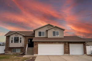 View of front of property with a garage, driveway, brick siding, and fence