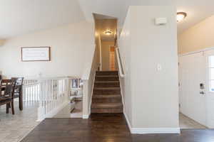 Stairs featuring plenty of natural light, vaulted ceiling, and wood finished floors