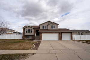 Tri-level home with concrete driveway, brick siding, a front lawn, and fence