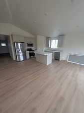 Kitchen with lofted ceiling, stainless steel appliances, a center island, light wood finished floors, and light countertops