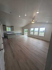 Unfurnished living room featuring wood finished floors, a ceiling fan, a sink, lofted ceiling, and recessed lighting