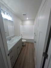 Full bath featuring toilet, visible vents, vanity, bathtub / shower combination, and wood finished floors