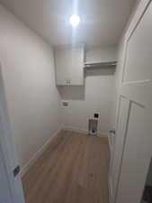 Clothes washing area with light wood finished floors, washer hookup, cabinet space, and baseboards