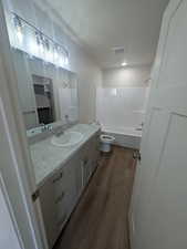 Bathroom featuring toilet, wood finished floors, vanity, visible vents, and tub / shower combination