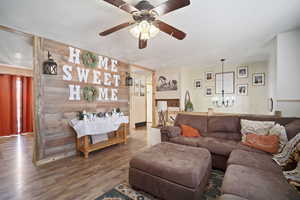 Living room with a textured ceiling, ceiling fan with notable chandelier, and wood finished floors