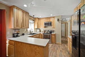Kitchen featuring stainless steel appliances, light countertops, a sink, light wood-type flooring, and a peninsula