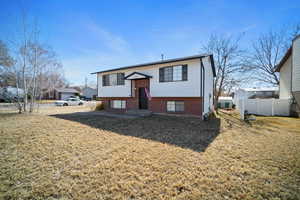 Raised ranch with a front yard, brick siding, and fence