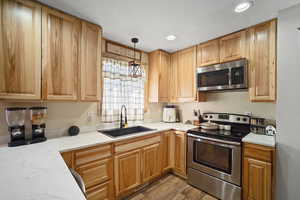 Kitchen featuring light wood finished floors, recessed lighting, hanging light fixtures, appliances with stainless steel finishes, and a sink