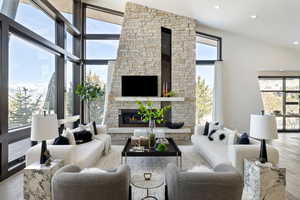 Living area featuring light wood-style floors, a healthy amount of sunlight, a stone fireplace, and a towering ceiling