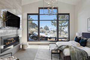 Carpeted bedroom featuring lofted ceiling, multiple windows, a notable chandelier, and a tile fireplace