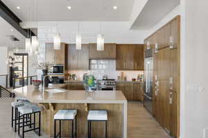 Kitchen featuring modern cabinets, a kitchen breakfast bar, built in appliances, pendant lighting, and a sink