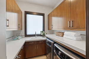 Kitchen with brown cabinetry, dishwashing machine, washing machine and clothes dryer, light countertops, and a sink