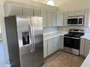 Kitchen with stainless steel appliances, light wood-type flooring, and light stone countertops