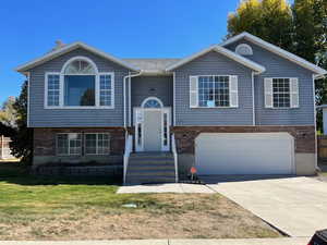 Raised ranch with an attached garage, driveway, brick siding, and a front yard