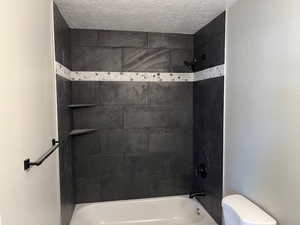Bathroom with a textured ceiling, bathtub / shower combination, and toilet