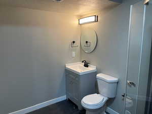 Bathroom featuring a textured ceiling, toilet, vanity, baseboards, and a shower with door