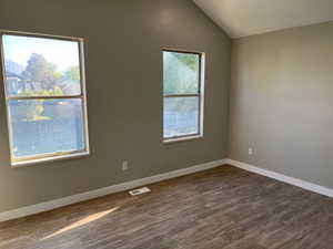 Bedroom featuring lofted ceiling, visible vents, baseboards, and wood finished floors
