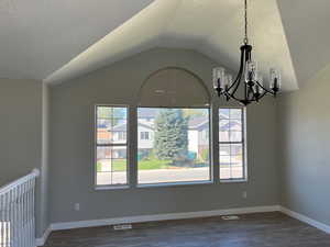 Unfurnished dining area featuring dark wood finished floors, visible vents, vaulted ceiling, a textured ceiling, and baseboards