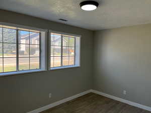 Spare room featuring visible vents, a textured ceiling, baseboards, and dark wood-style flooring