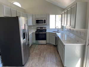 Kitchen with light wood finished floors, vaulted ceiling, a textured ceiling, stainless steel appliances, and a sink