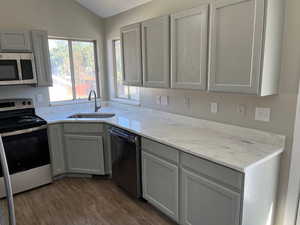Kitchen featuring dark wood-type flooring, vaulted ceiling, stainless steel appliances, gray cabinetry, and a sink