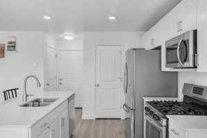 Kitchen with light wood-style flooring, stainless steel appliances, light countertops, white cabinetry, and a sink