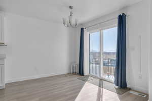 Unfurnished dining area with baseboards, light wood-style flooring, visible vents, and an inviting chandelier