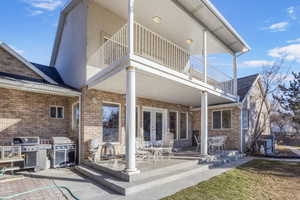 Rear view of property featuring brick siding, french doors, a patio area, and a balcony