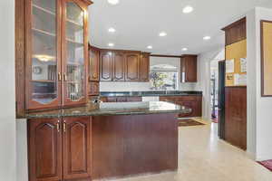 Kitchen with a peninsula, dark stone countertops, arched walkways, and glass insert cabinets