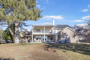 Back of property featuring a patio, a balcony, a chimney, central AC, and brick siding