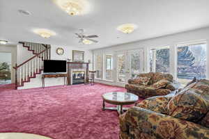 Living area with carpet, stairway, a wealth of natural light, and a glass covered fireplace