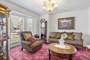 Carpeted living room featuring a notable chandelier, a textured ceiling, and baseboards