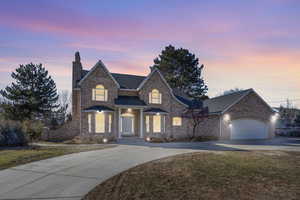 View of front of home featuring an attached garage, brick siding, driveway, a chimney, and a front yard
