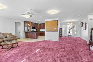 Living room featuring arched walkways, visible vents, light carpet, a textured ceiling, and ceiling fan with notable chandelier