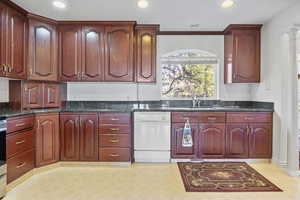 Kitchen featuring reddish brown cabinets, light floors, white dishwasher, a sink, and ornate columns