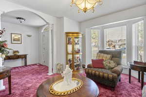 Living area featuring arched walkways, a textured ceiling, a chandelier, carpet flooring, and decorative columns