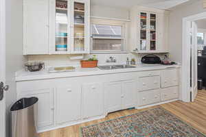 Kitchen with light wood-style flooring, glass insert cabinets, light countertops, and a sink