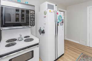 Kitchen with light wood-type flooring, white appliances, baseboards, and visible vents