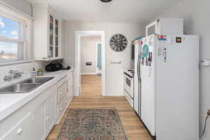 Kitchen with glass insert cabinets, light wood-style floors, white cabinetry, a sink, and white appliances