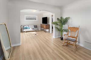 Sitting room featuring light wood-type flooring, arched walkways, visible vents, and baseboards