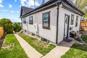View of property exterior with fence, a lawn, a chimney, and entry steps