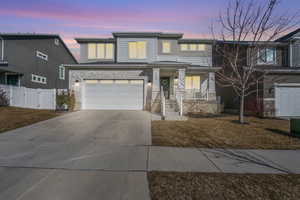 View of front of home featuring a garage, fence, concrete driveway, stone siding, and a gate