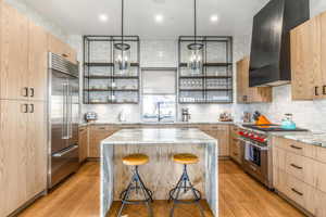 Kitchen with open shelves, a kitchen island, wall chimney range hood, light brown cabinetry, and high end appliances