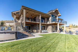 Back of property with a yard, a patio, a hot tub, stone siding, and stairs